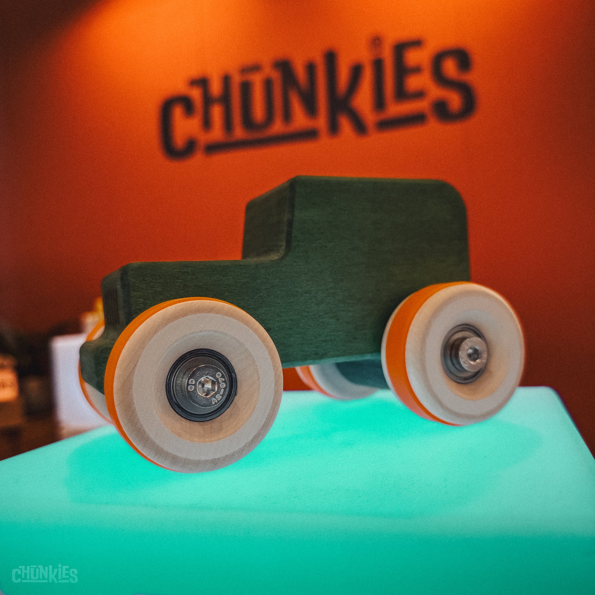 Wooden toy car with chunky wheels on a teal surface, branded 'Chunkies' in the background. Chunkies wooden toy cars come with two sets of tires to customize to your liking.